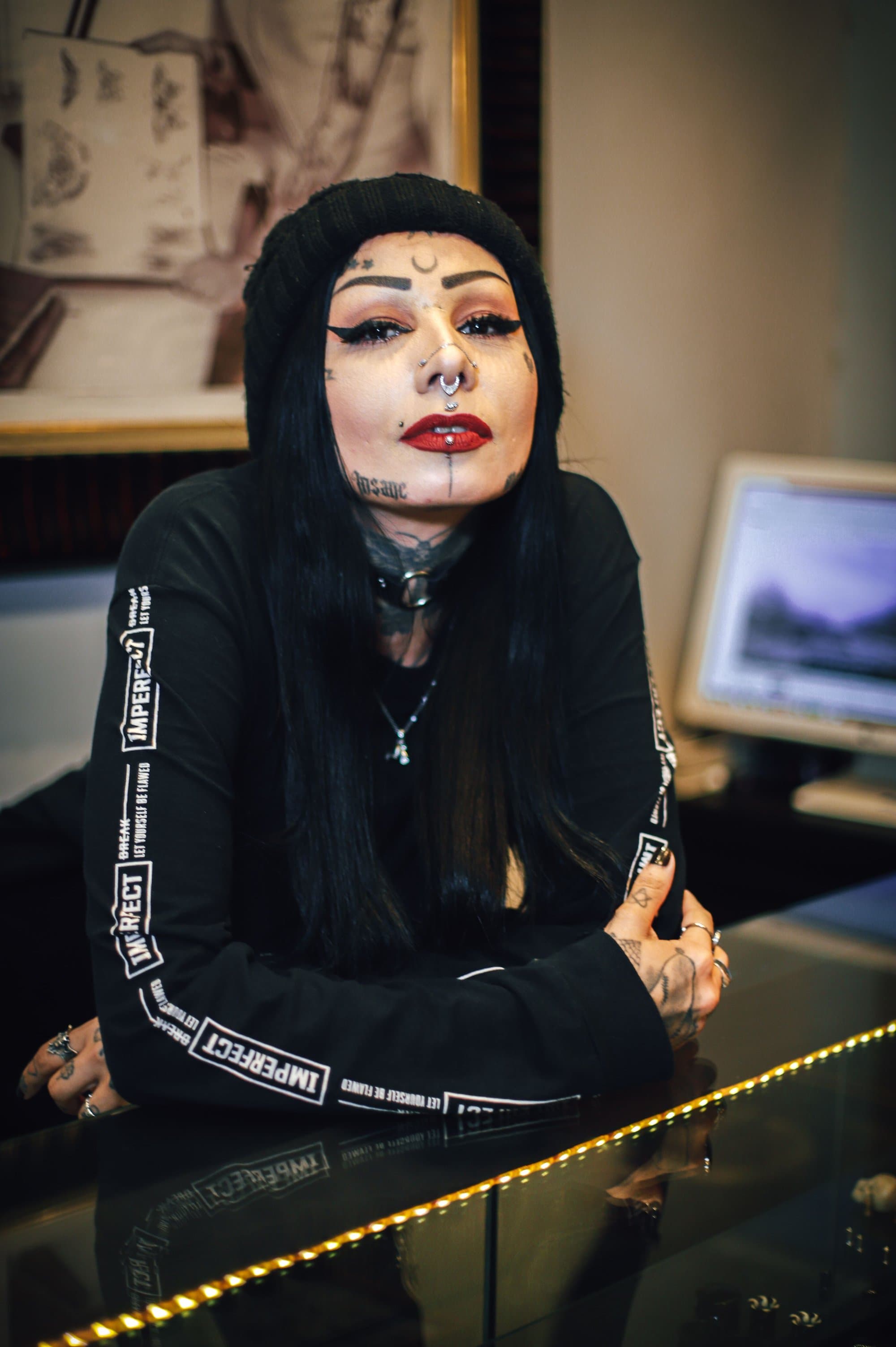 Tätowierte Person mit Piercings sitzt im Studio am Schreibtisch